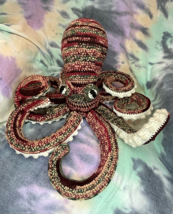 crochet octopus made of variegated maroon, green and beige yarn.