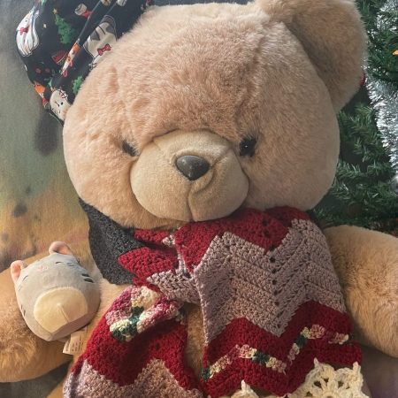 A large teddy bear wearing a scarf with snowflakes